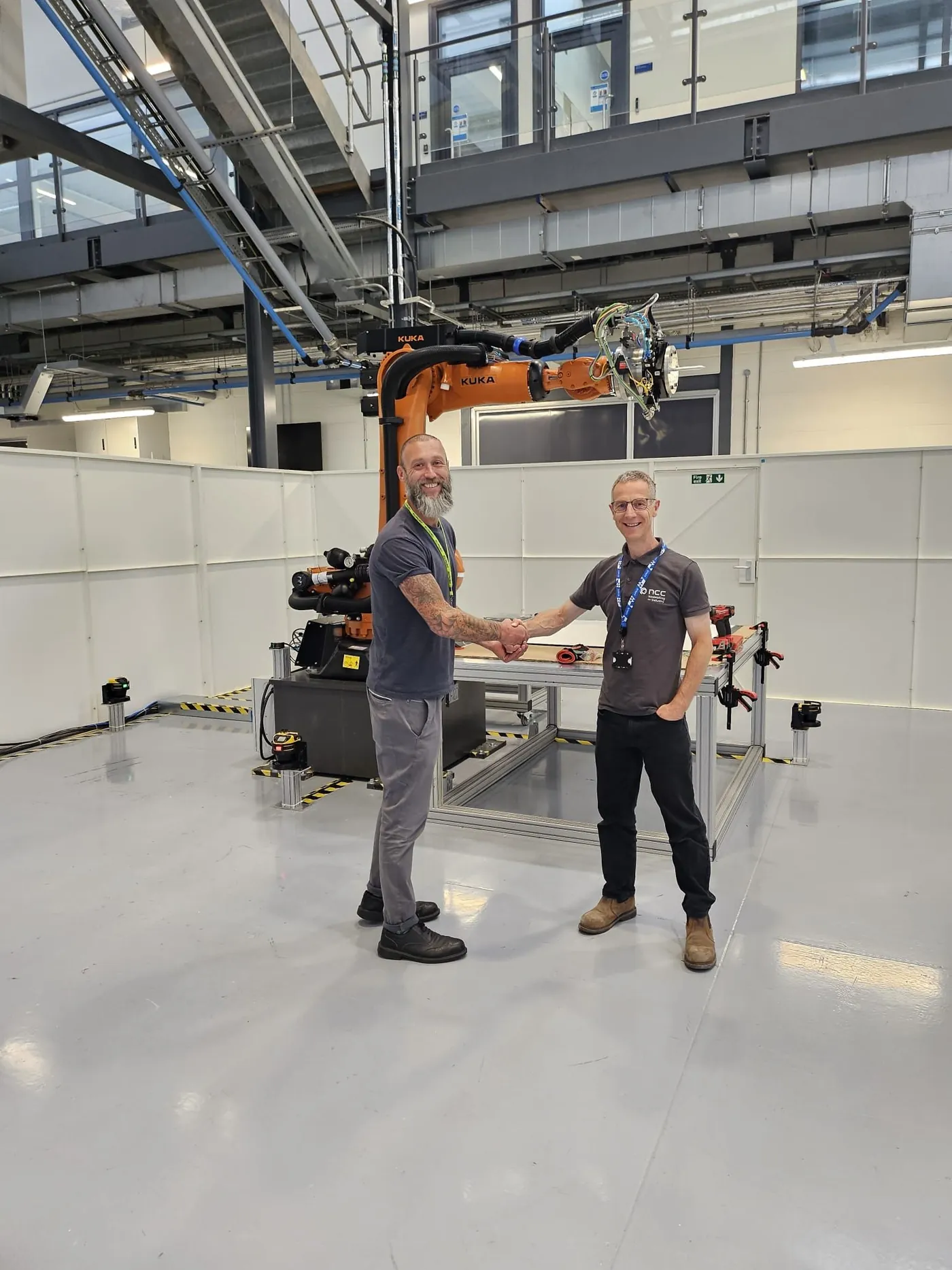 Orion engineer shaking hands with an NCC engineer in front of the moveable KUKA robot cell for carbon-fibre cutting
